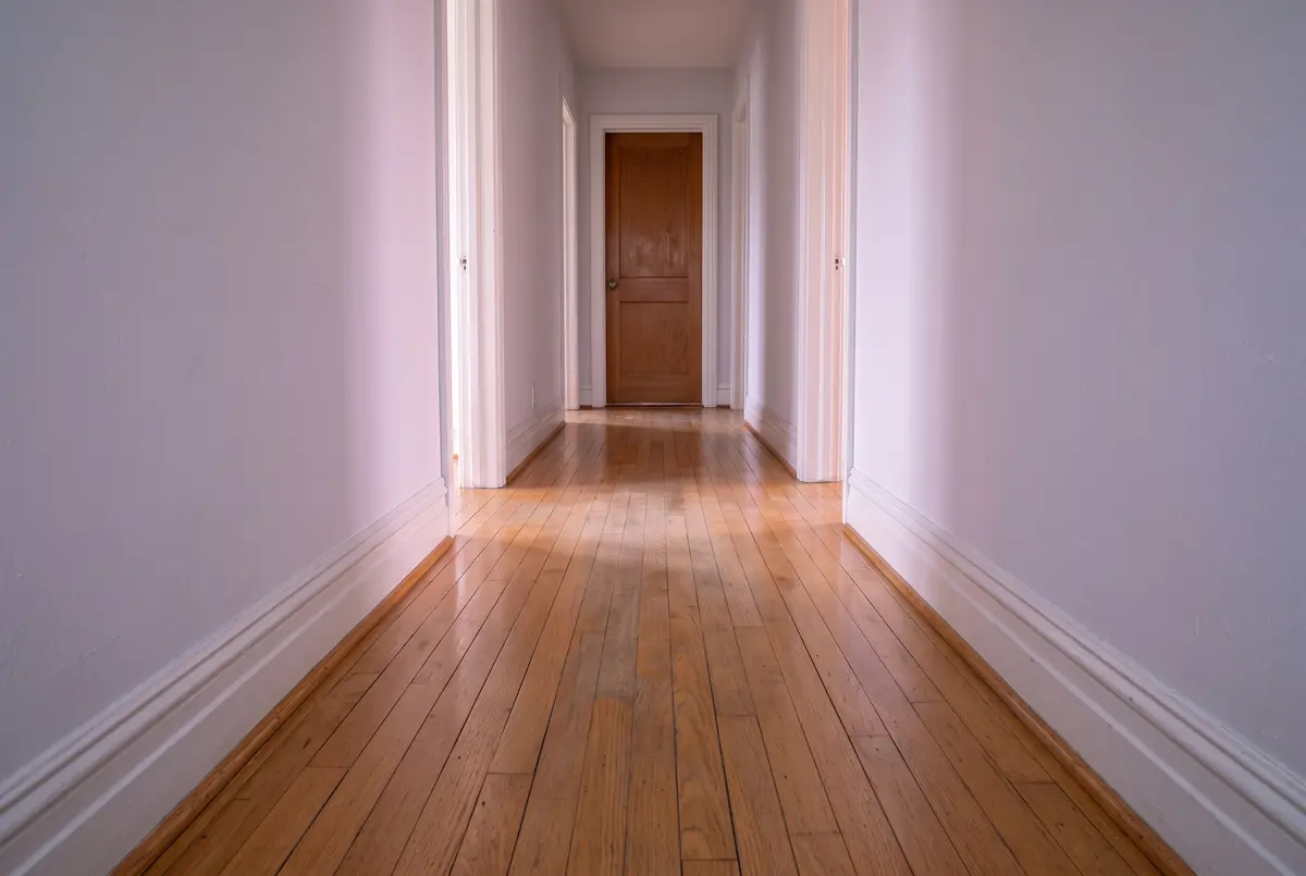 Illustration of a hallway in an older house with narrow original oak floorboards, the finish dull and pale down the middle where people walk and still glossy along the walls.