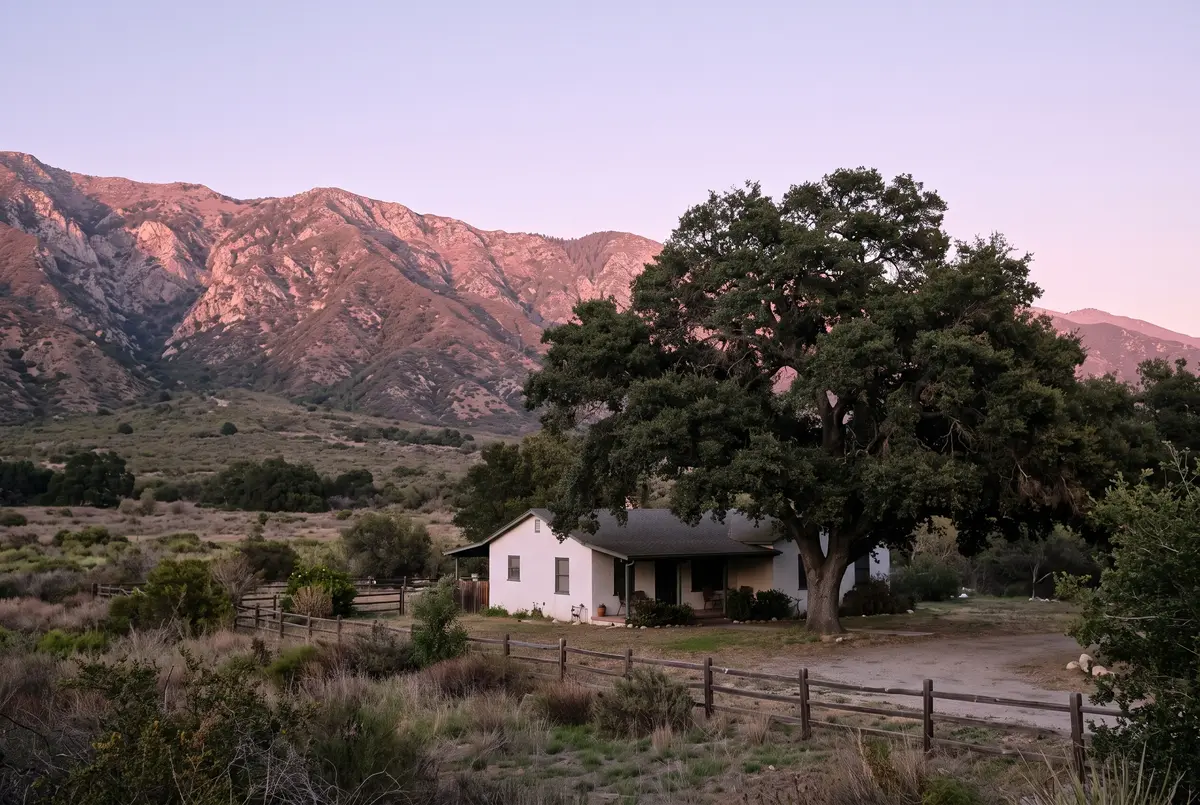 Illustration of a single-story valley house under a broad oak, with the mountain ridge behind it glowing pink at sunset.
